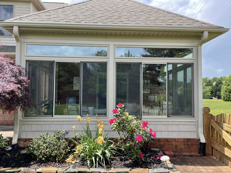 Sunlight floods a welcoming sunroom overlooking a vibrant garden bursting with colorful blooms and greenery.