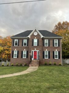 A stately brick house with striking windows stands amid autumn trees beneath a brooding, clouded sky.