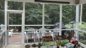 A cozy screened porch with plants and a table overlooks a peaceful, sunroom-like wooden deck.