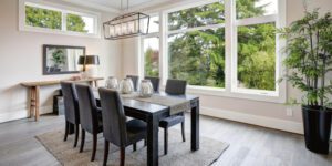 A sleek black dining table anchors a bright, serene room overlooking trees through expansive windows.